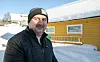 Mann i vinterklær står foran gult hus omgitt av snø i solskinn.