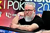 Mann med briller og skjegg sitter ved pokerbord under pokerturnering innendørs.