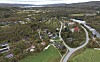 Luftfoto av bygdesamfunn med hus, vei, elv og jorder omgitt av skog.
