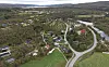 Luftfoto av bygdesamfunn med hus, vei, elv og jorder omgitt av skog.
