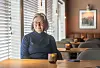 Eldre kvinne med briller sitter alene ved et bord på en rolig kafé med tente lys.