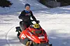 Ung gutt sitter på rød racingsnøskuter med startnummer 518 på snødekt bane.