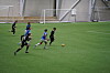 Fotballspillere løper etter ballen på kunstgress i innendørs fotballhall.