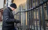 Person i mørke klær arbeider ved en høy smijernsport foran en gul murbygning.