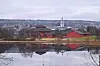 Rørosbebyggelse og kirketårn speiler seg i et stille vann en overskyet dag.