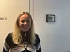 Smilende kvinne med navnesnor foran lys vegg med lite bilde