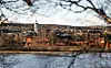 Utsikt over en by med røde bygninger, kirketårn og vann i forgrunnen.