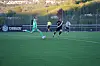 Fotballspillere i grønt og svart løper på en kunstgressbane under en kamp.