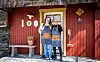 To personer står foran et rødmalt bakeri med gule dører, skilt og en benk ved inngangen. Ida Rambraut Tove Gløtheim