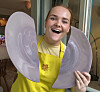En smilende person i gul forkledning holder to store, hvite fat innendørs. Ida Rambraut