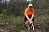 Trener med gul hjelm holder en ettersøkshund i skogen.