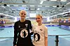 To ungdommer står smilende i en håndballhall foran en blå spilleflate og tribuner.