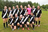 En gruppe jenter i svarte fotballdrakter står og kneler på en gressbane utendørs.