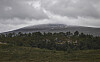 Lavt fjell under mørke skyer med skogkledd landskap i forgrunnen.