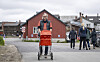 Mann triller en bagasjevogn med oransje bagasje foran en rød bygning.
