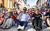 En gruppe mennesker sitter på asfalten i en gate og beveger armene i takt.