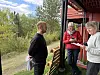 Tre personer snakker sammen ved en rød bygning omgitt av grøntområder.