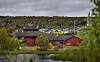 Rødt trehus ved en dam med trær, åser og overskyet himmel.