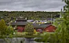 Rødt trehus ved en dam med trær, åser og overskyet himmel.