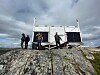 Personer ved et solcelleanlegg på en steinete fjellrygg under mørke skyer.
